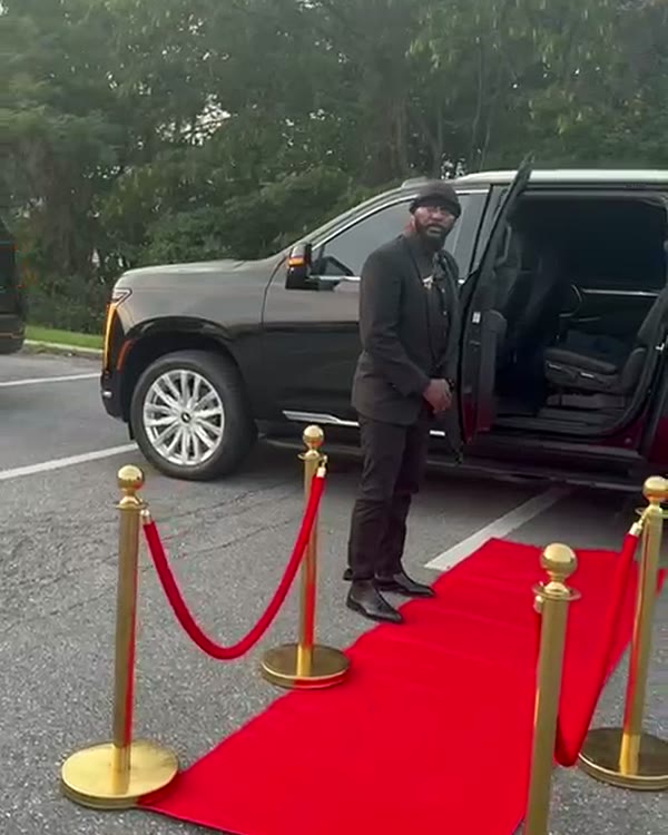 Black Cadillac Escalade parked beside a red carpet lined with gold stanchions and red rope