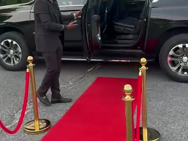Red carpet runner between gold stanchions leading to a black SUV with its rear door open